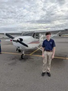 Parker standing in front of a small propeller plane on the airport tarmac