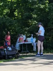People gathered around the lemonade stand beside a shaded walking path