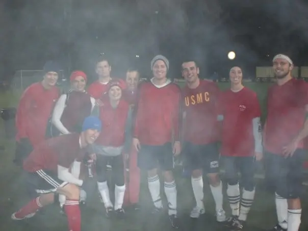 Adult soccer teammates in red jerseys posing together after a night game