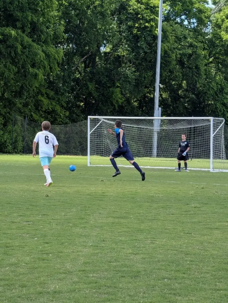 Soccer player in a white number six jersey approaching a blue ball near the goal